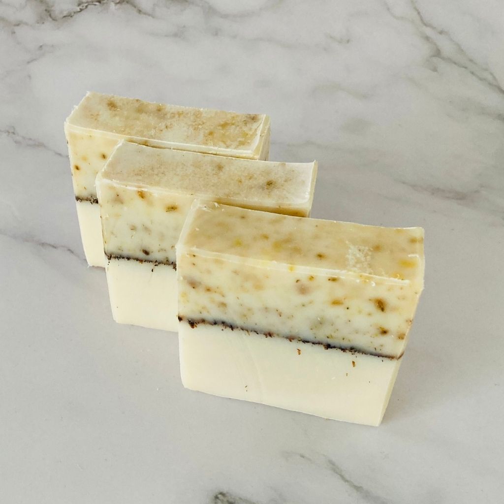 pure & pretty Dhana Soap bar RTSB01 has yellow variation on the top a black line across the middle and white on the bottom. Three bars of soap sit in a row. The soap is unscented with ground chamomile flowers.