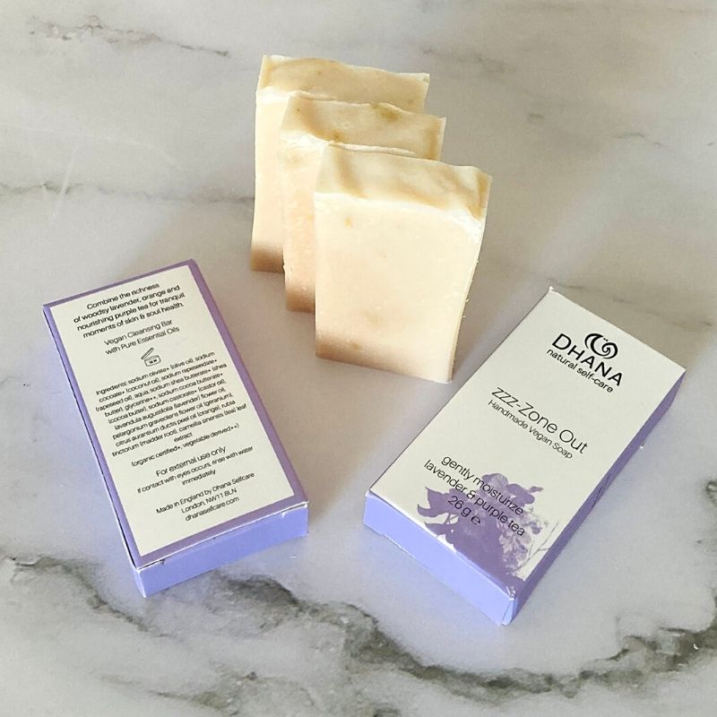 RTSB-s01 Miniature zzz-Zone Out Bars of Soap. A collection of 2 purple and white boxes laying on a marble background. Three bars of pale pink lavender soap sit between them.