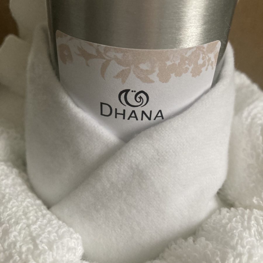 aluminum bottle wrapped in flannel and nestled in towel. Label simply reads Dhana with peach botanical motif.