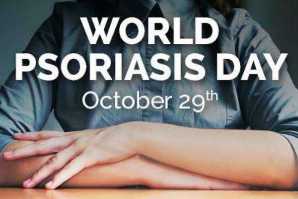 close up of a woman with arms crossed on a table. We see her bleu shirt as a background for the words "World Psoriasis Day" Oct 23rd