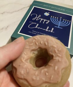 hand holding a pink and brown donut soap. It's box is in the background reading Happy Chanukkah on a marble backdrop