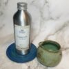 Metal castor oil bottle on blue coaster with small green jug on marble background